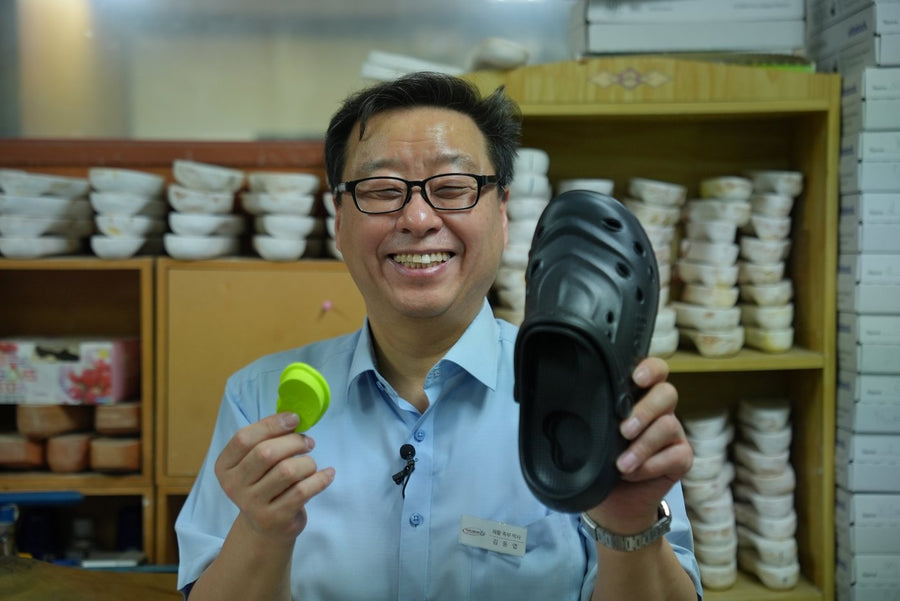 Dr. Dongyeop Kim in his workshop, holding a black pipiu clog and the green Peanut Pad, shelves of foot molds behind him