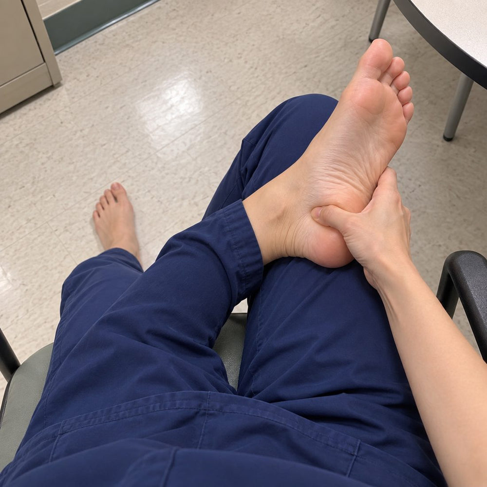 Nurse in navy scrubs on a break, barefoot, pressing her thumb into her heel
