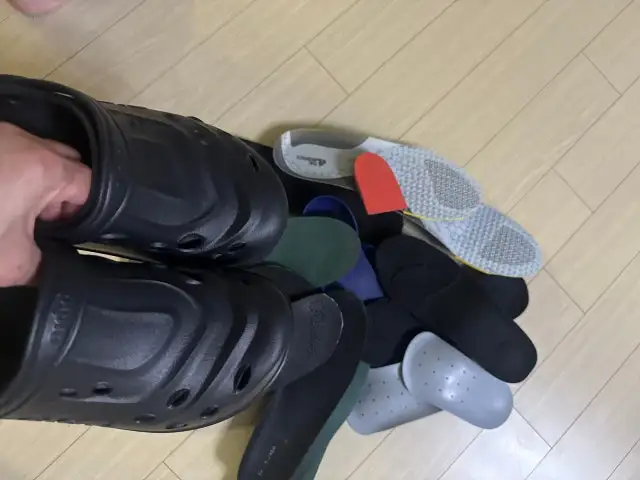 Black pipiu clogs held above a pile of insoles the reviewer had tried before